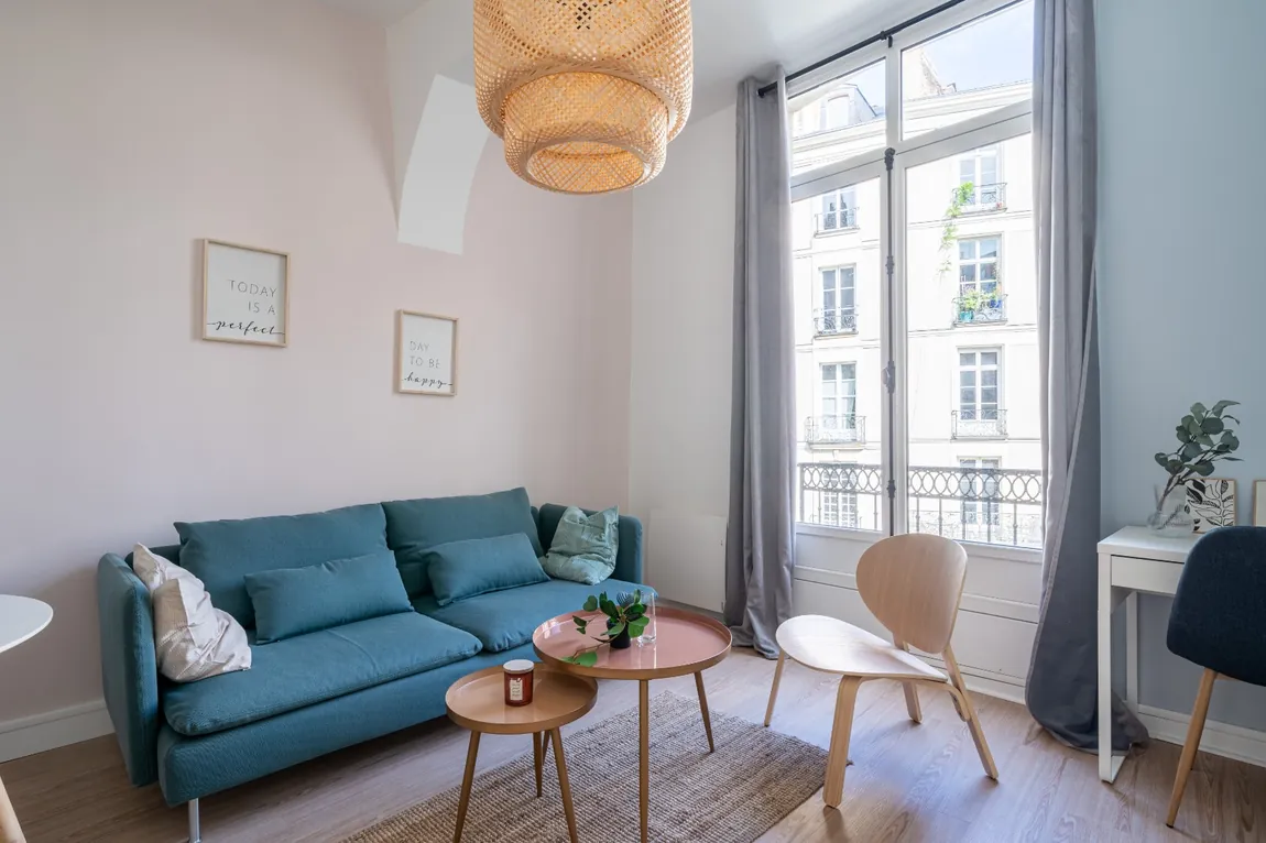 Salon d’un appartement ancien avec canapé bleu, suspension et grande fenêtre.