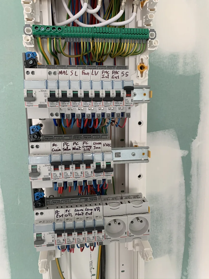 Tableau électrique ouvert en cours de réalisation, avec conducteurs organisés et circuits repérés.